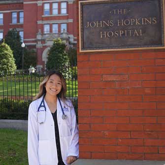 Smiling student stands by Johns Hopkins sign.