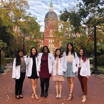 A group of friends stands smiling on Johns Hopkins campus in fall.