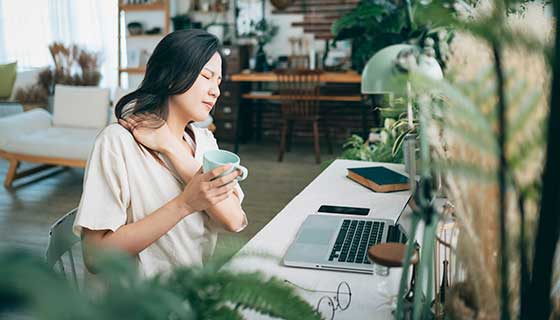 Woman suffering from neck pain while working from home.