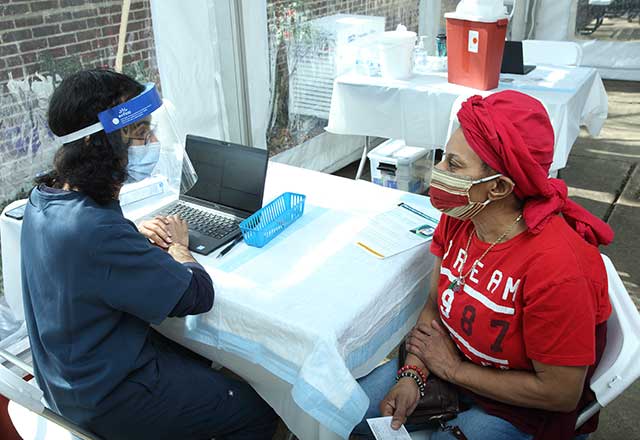 Healthcare providing discussing vaccine outside community member's apartment.