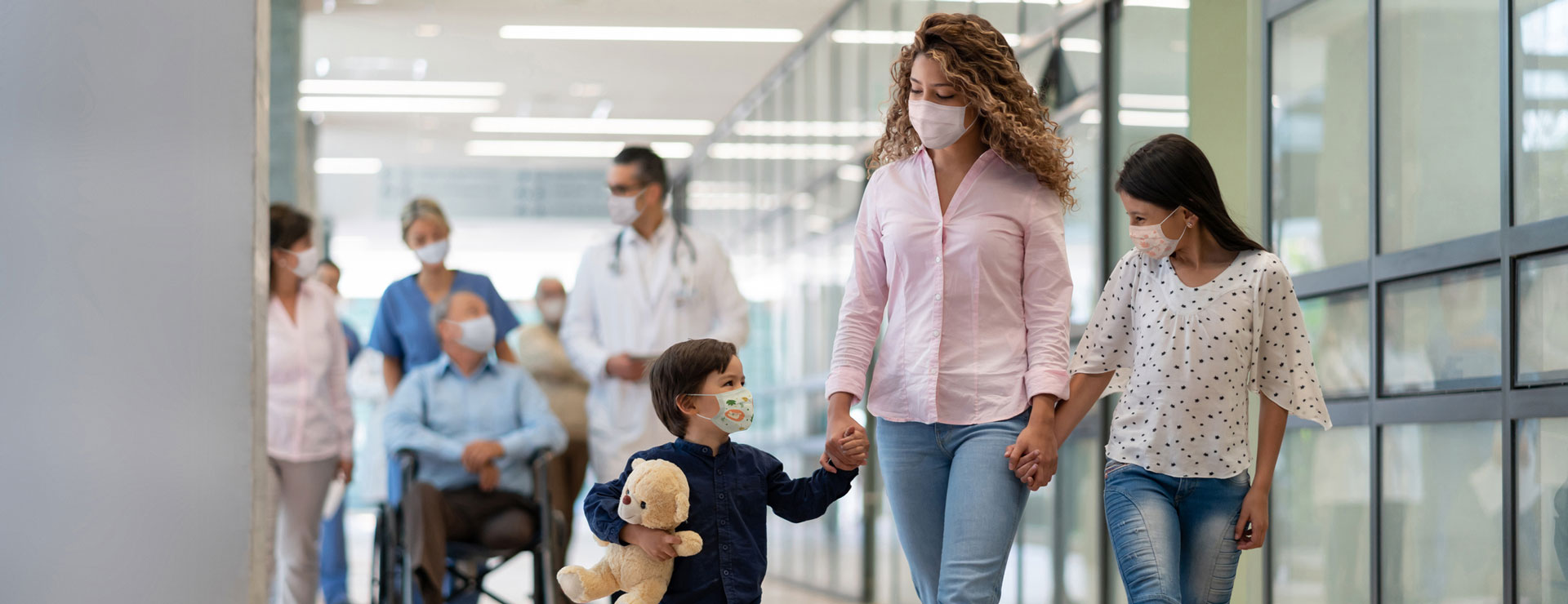 A woman walks with her children inside of a medical facility with masks on.