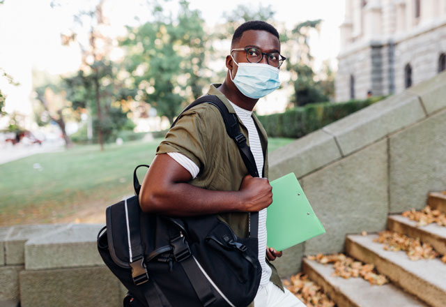 A young man with a backpack on and books in hand.