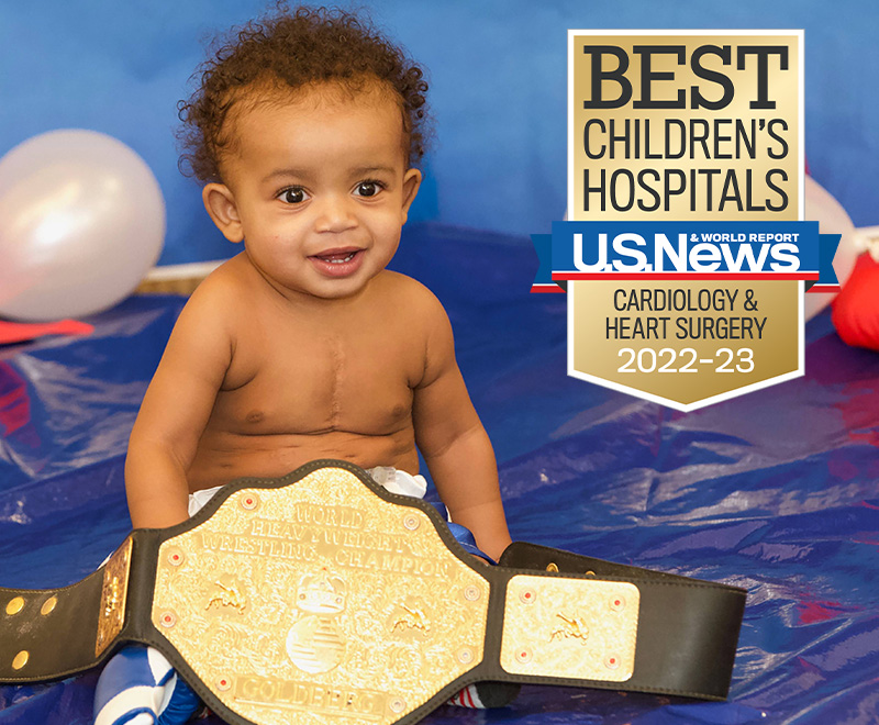 A smiling baby sitting behind a wrestling championship belt.