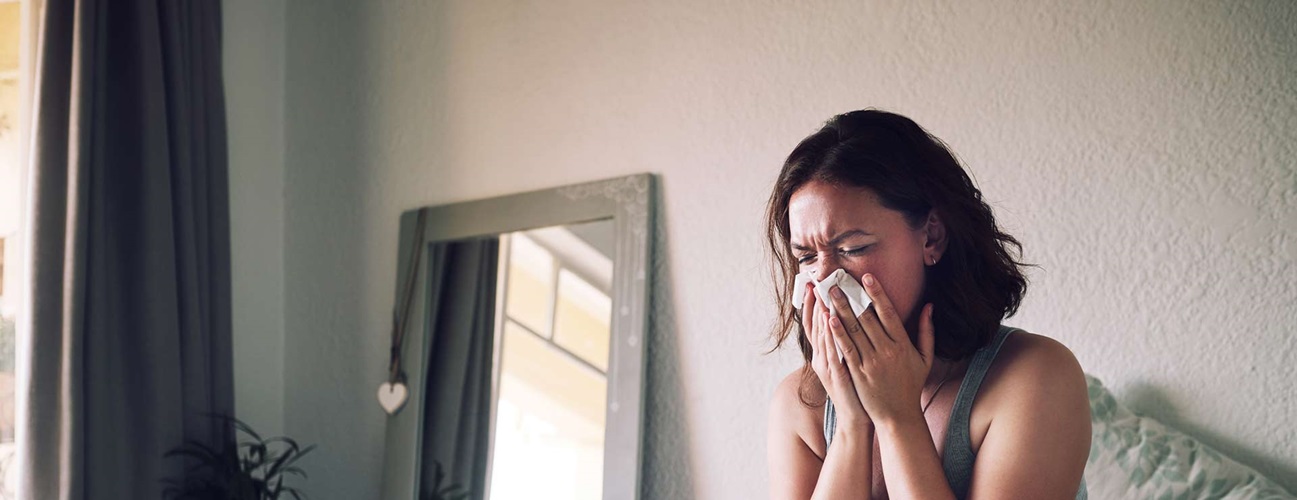 Woman sitting upright, coughing into a tissue