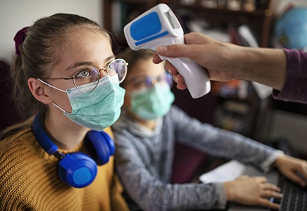 Masked young adult gets temperature checked.