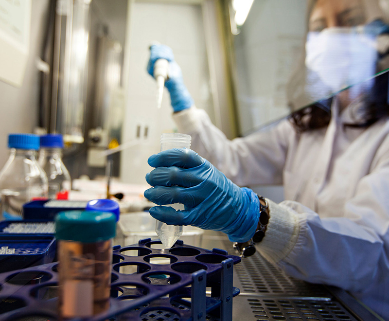 A scientist uses a pipette while wearing a mask.