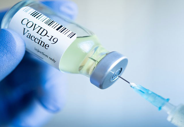 a gloved hand holding a COVID-19 vaccine vial and syringe