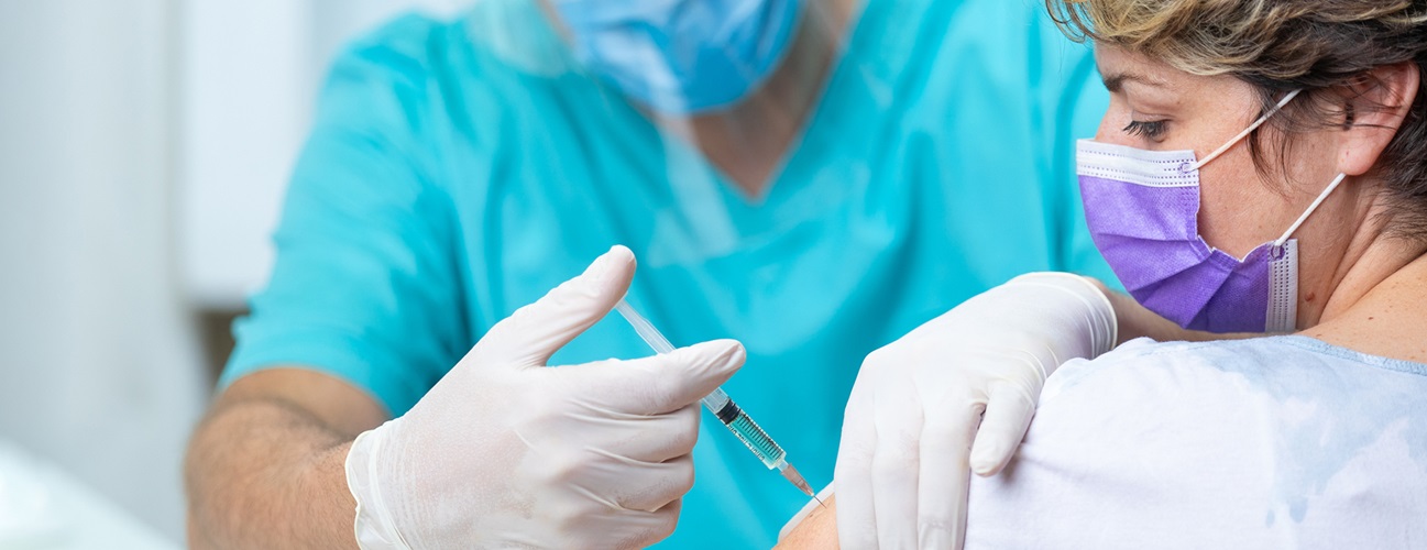 A doctor vaccinates a patient; both are wearing masks.