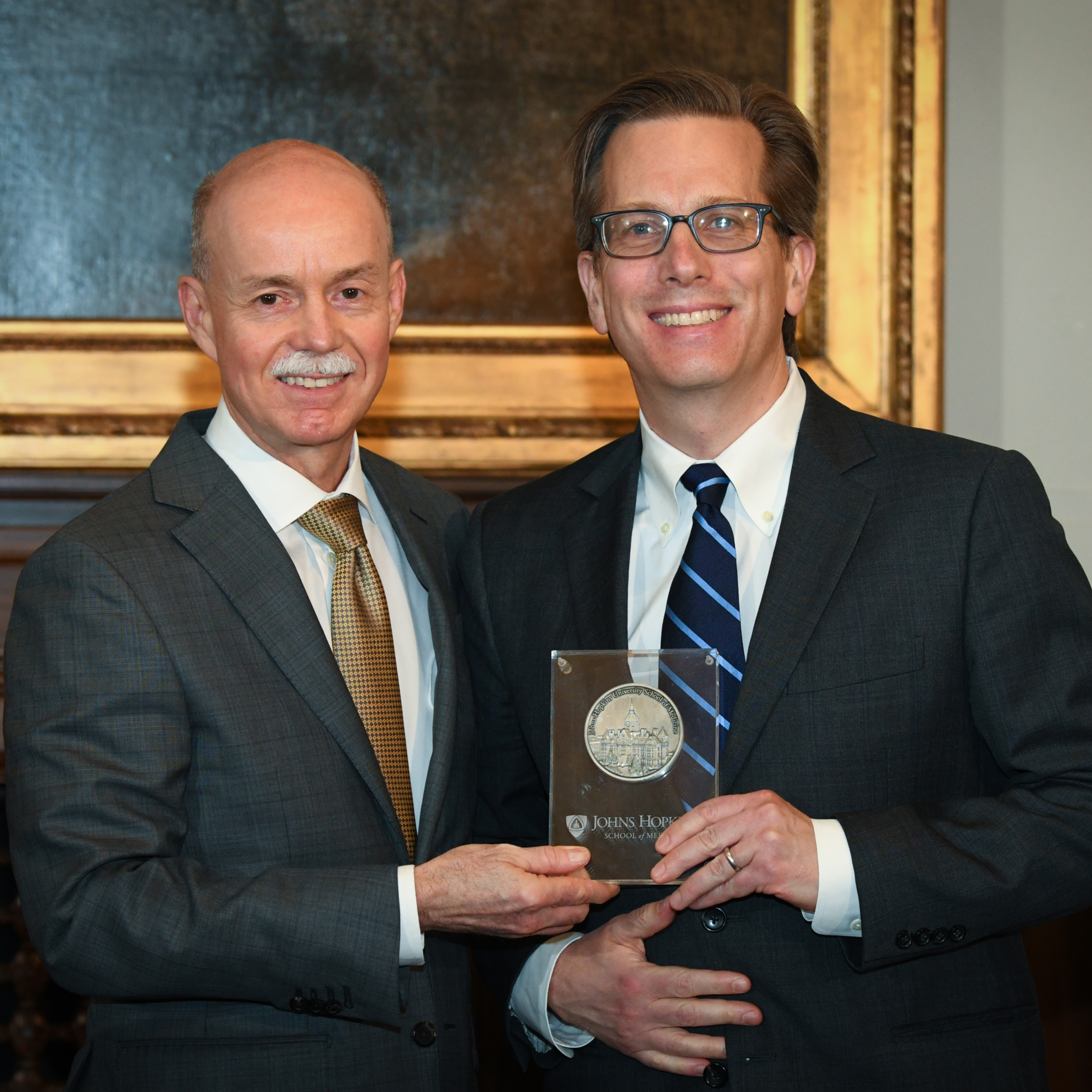 Andy Ewald and Ted Deweese holding a commemorative plaque at the Virginia DeAcetis Professorship dedication