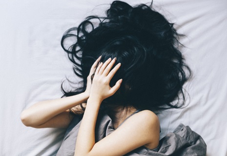 A woman in bed covering up her face with her hair.