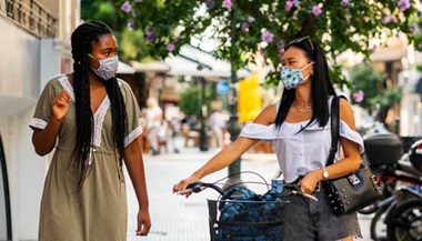 Two women walk down the street together wearing masks