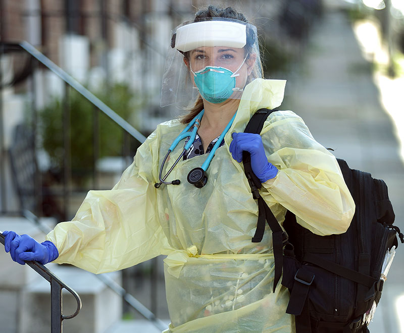 a home care nurse in PPE stands outside of a patient's house