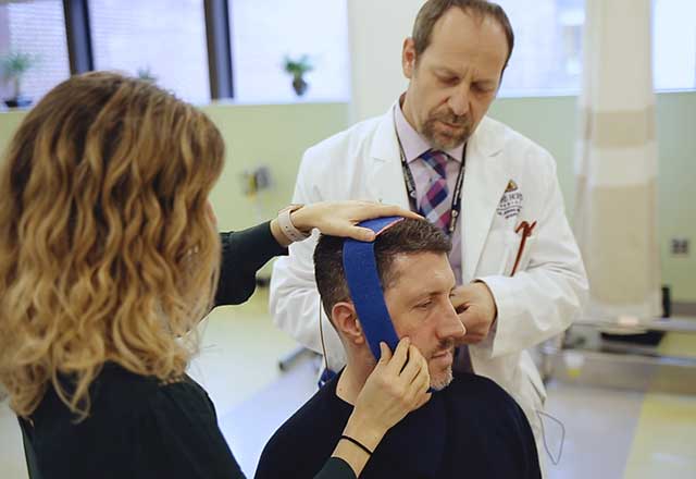 Dr. Pablo Celnik and a physical therapist applying electrodes to Michael's head