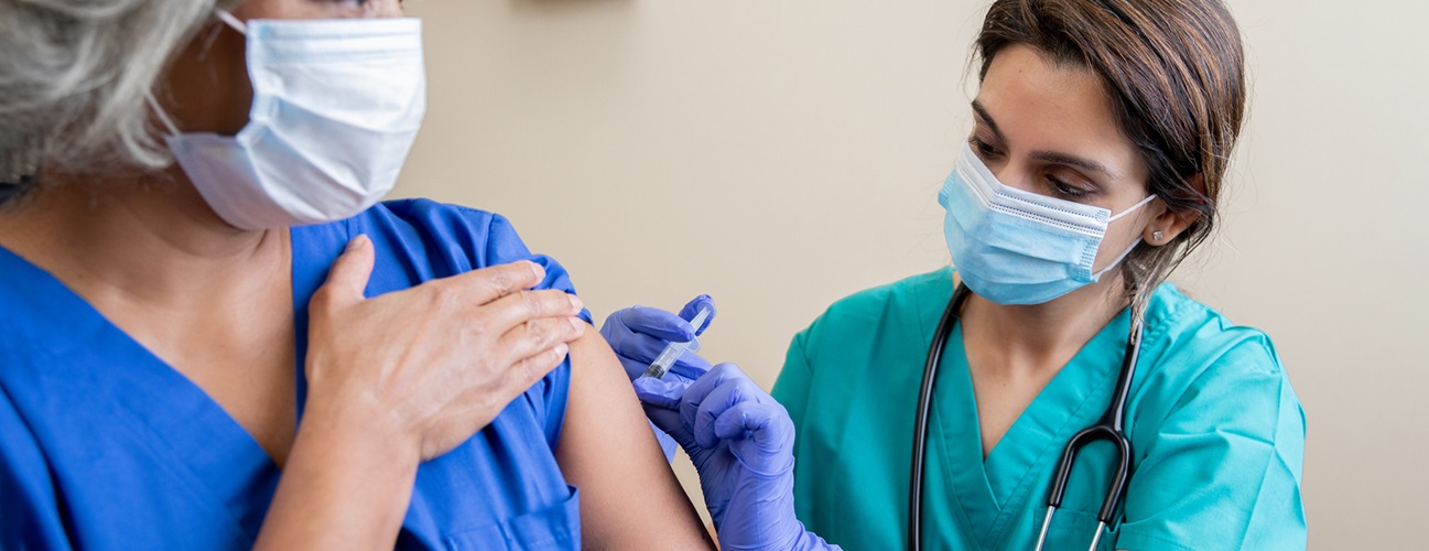 An older African American woman receives a vaccination from her healthcare provider.