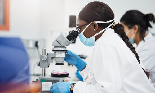 Masked researcher looking into a microscope