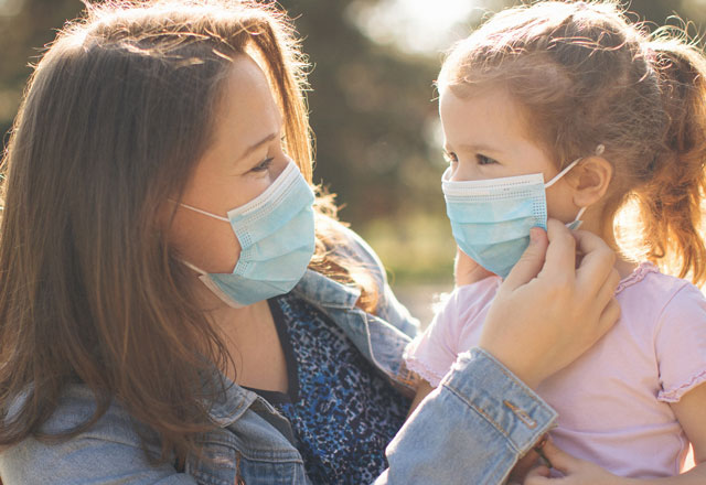 A mother and a child wear masks while outdoors.