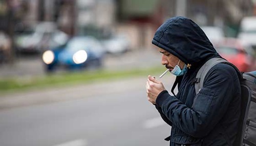 Man with mask pulled down, smoking.