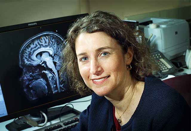 Dr. Susakauer sitting in front of a computer that has a brain x-ray shown on it.