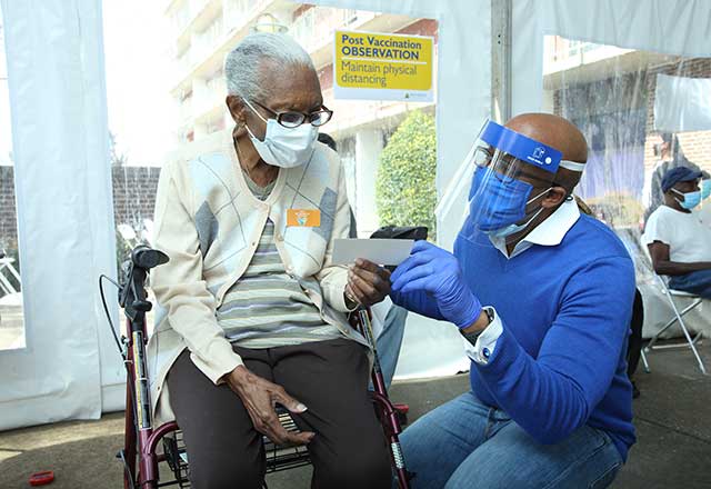 Healthcare provider explaining the COVID-19 vaccination card to elderly person.