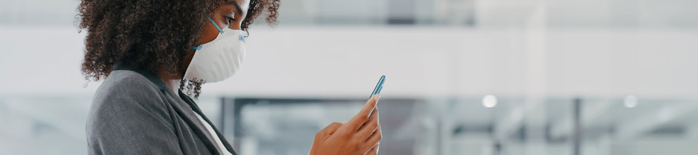 A young woman checks her phone while wearing a protective mask.