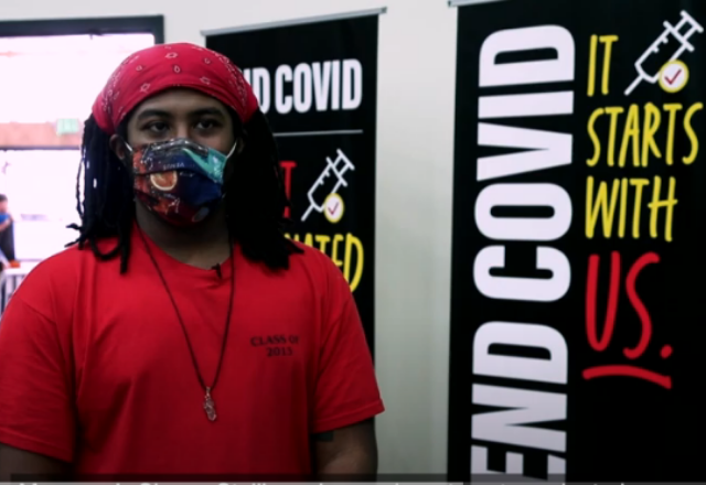 screenshot from video, man standing in front of vaccine center sign